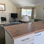 Open-plan sitting room and kitchen in a Brooklands cottage apartment, with fireplace and dining area