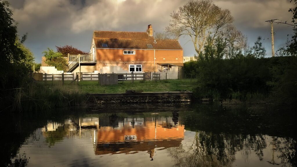 The brick farmhouse at Brooklands housing the two self-catering cottage apartments, reflected in the fishing lake at sunset