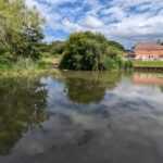 Still water on the lake at Brooklands reflecting the sky and the farmhouse